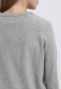 Svetlo sivi pulover iz mehke pletene tkanine. Ima okrogel izrez in subtilno teksturo, raglan rokave ter čist zaključek.