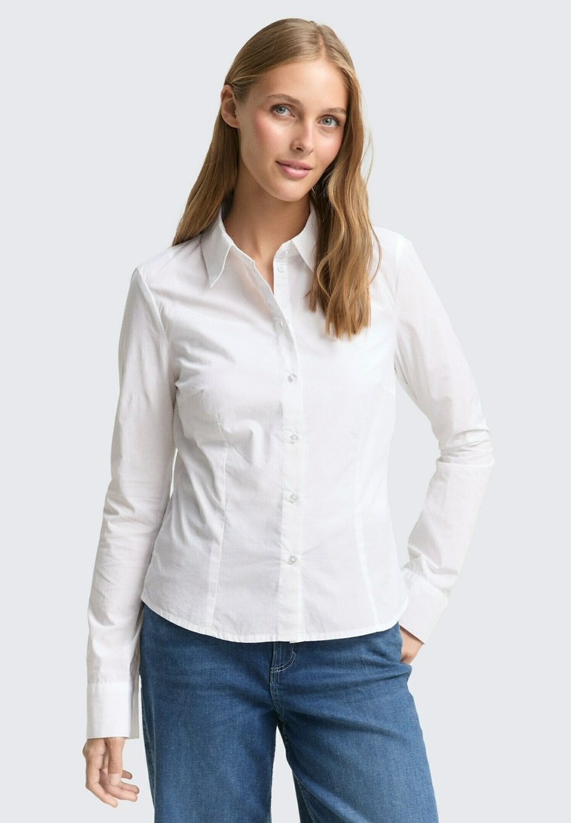 Witte overhemd met lange mouwen, voorzien van een puntige kraag en een getailleerd ontwerp. Gladde textuur, lichtgewicht stof. Blauwe denim jeans gedragen.