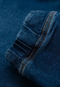 Tela de mezclilla azul con un puño fruncido, que presenta un visible detalle de costura naranja a lo largo de la costura, destacando textura y diseño.