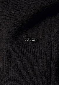 Czarny dziergany sweter o prążkowanej fakturze z małą czarną metką z nazwą marki "Scotch & Soda" umieszczoną z boku.