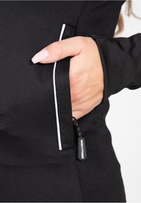 Chaqueta atlética negra con un bolsillo con cremallera y una pestaña para tirar, ribete blanco en el bolsillo y un detalle texturizado en la manga.