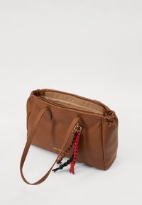 Brown leather handbag with a textured finish, featuring two long handles and a decorative tassel in red and black. Gold zipper closure.