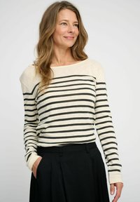 Gestreiftes Langarmshirt in Creme mit schwarzen horizontalen Streifen, mit entspanntem Schnitt, weitem Ausschnitt und gerippten Bündchen. Kombiniert mit schwarzen Hosen.