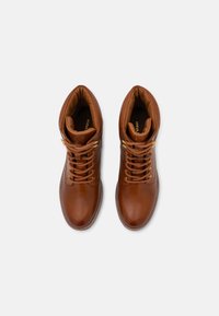 Bottines en cuir marron avec bouts ronds, présentant un laçage à l'avant, des accessoires en métal doré, un col rembourré et une texture lisse.
