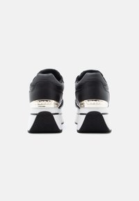 Baskets noires avec une tige en cuir lisse, semelle blanche épaisse et accent métallique sur le talon. Semelle extérieure en caoutchouc texturé noir pour une meilleure adhérence.