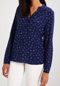 Blusa a maniche lunghe blu navy con piccolo motivo floreale bianco, pattina con bottoni e vestibilità comoda. Tessuto morbido con una texture liscia.
