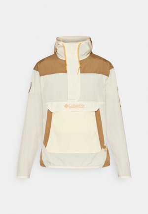 Veste anorak crème et marron, avec une poche avant, capuche réglable avec cordon de serrage, et accents jaunes contrastants. Matériau léger.