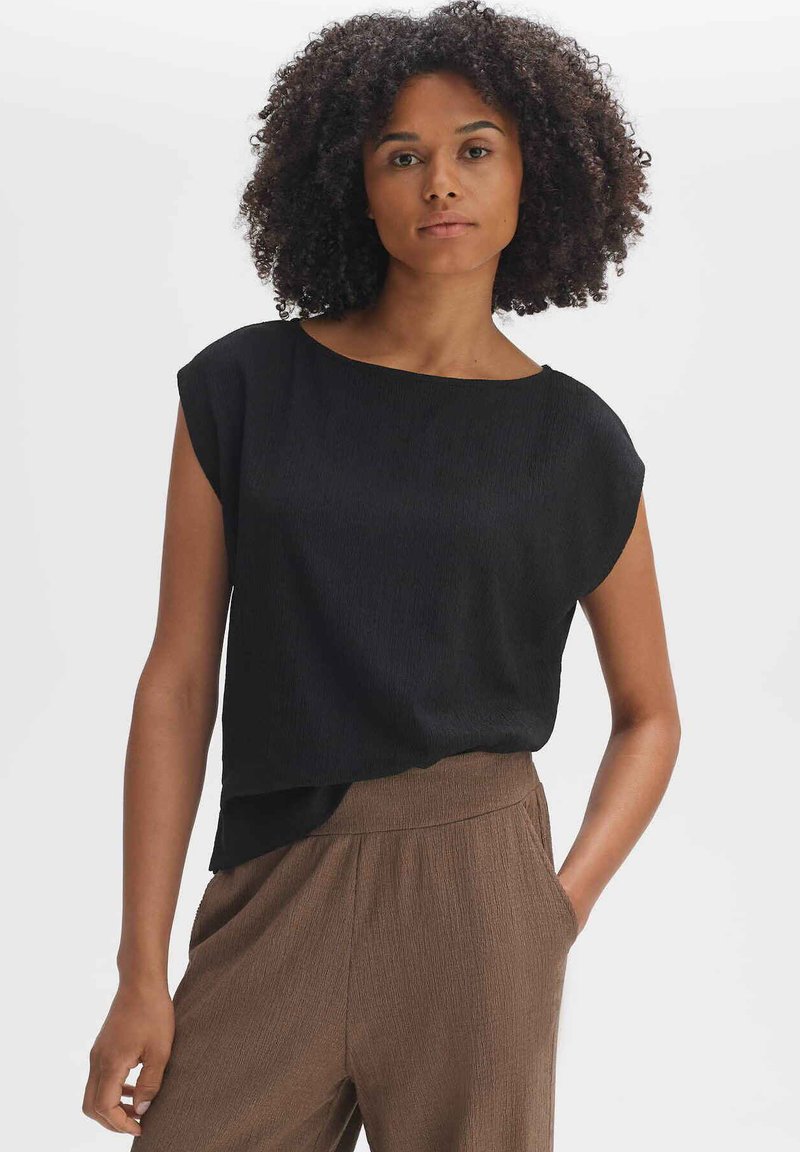 Schwarzes kurzärmliges Oberteil mit strukturierter Oberfläche und lockerer Passform, kombiniert mit braunen, plissierten Hosen mit Seitentaschen.