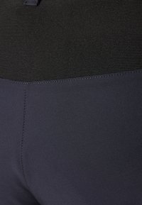 Leggings deportivos oscuros con una cintura texturizada negra, tela suave debajo y costuras ordenadas a lo largo de las uniones.