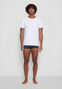 Camiseta branca de manga curta em mistura de algodão, combinada com boxers azul-escuro. O modelo está descalço contra um fundo simples.