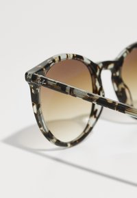 Gafas de sol redondas con montura de carey oscuro y lentes marrones degradados. Presentan un acabado delgado y brillante con un sutil logotipo de la marca.