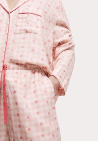Rosa rutig pyjamasset med små röda hjärtan, långa ärmar, en bröstficka och ett elastiskt midjeband med en rosa dragsko.