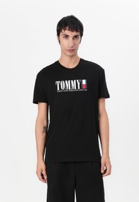 Svart bomulls T-skjorte med "TOMMY" logo i hvitt og rødt, rund hals, kort ermer, glatt tekstur og avslappet passform.