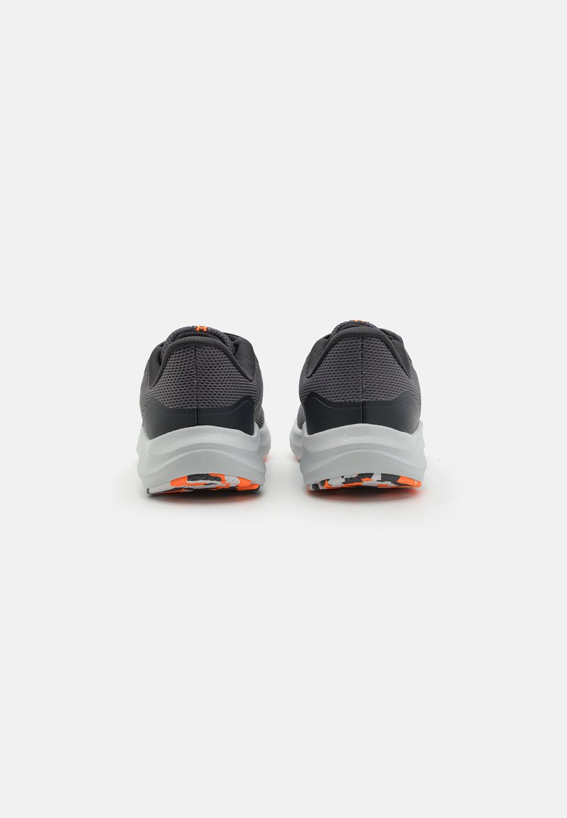 Baskets de sport grises avec une tige en maille texturée, semelle blanche et accents orange sur le talon et la semelle extérieure. Forme arrondie avec un col rembourré.