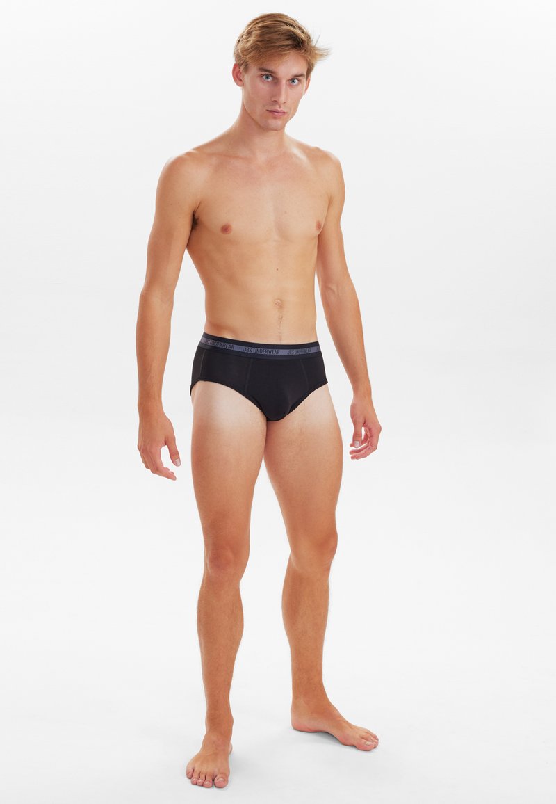 Sorte briefs-lignende undertøj med en kontrasterende grå elastik, glat stof og en tætsiddende pasform, præsenteret på en mandlig model i en neutral setting.