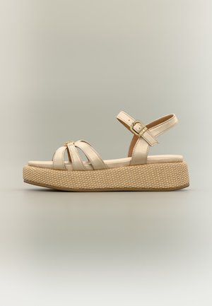 Πλατφόρμα πλατφόρμας σε μπεζ χρώμα με πλεγμένη σόλα, τρεις μπροστινές λουρίδες και λουρίδα αστραγάλου με χρυσή αγκράφα σε ουδέτερο φόντο.