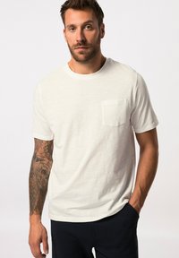 Camiseta blanca de algodón con cuello redondo y mangas cortas. Cuenta con un bolsillo en el pecho y una tela suave con una ligera textura.