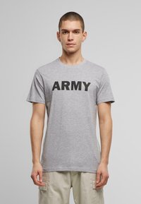 Pilkos medvilnės marškinėliai su trumpomis rankovėmis ir apvaliu kaklu, su ryškiu juodu užrašu "ARMY" ant krūtinės.