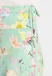 Kalhoty s květinovým potiskem v mentolové barvě, s žlutými, růžovými a fialovými květy. Obsahují boční zip a detailování sklady.