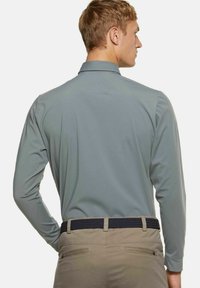 Herenhemdd met lange mouwen in lichtgrijs, met een zachte textuur en klassieke kraag, gecombineerd met beige broek en een donkere geweven riem.