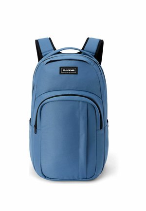 Zaino Dakine blu con spallacci imbottiti, tasca frontale con cerniera e maniglia superiore su sfondo bianco.