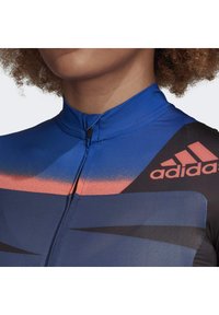 Cyklistická performance dres v modré barvě, s uzávěrem na zip, logem Adidas v růžové a grafickými vzory v tmavších odstínech.