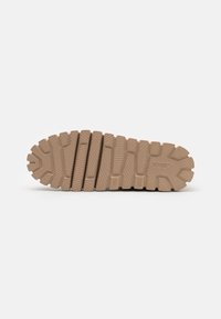 Suela de zapato de goma color beige con una superficie texturizada y con patrones que presentan surcos y crestas para mayor tracción. Detalle notable del logo en el lateral.