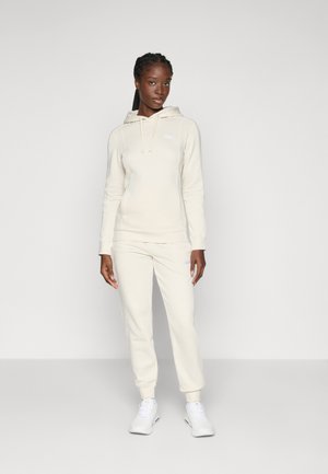 Hanorac bej cu șnururi și logo, asortat cu pantaloni tapered și adidași albi. Material neted cu o croială lejeră.