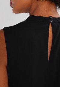 Haut sans manches noir avec une fente dans le dos et un détail de bouton, tissu lisse et design de décolleté épuré.