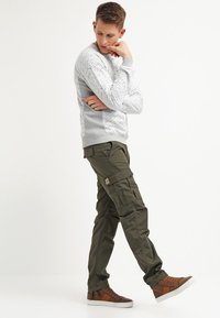 Grå teksturert sweatshirt med ribbede mansjetter, parret med olivengrønne cargo-bukser med flere lommer og et lite logo-merke. Brune sneakers.