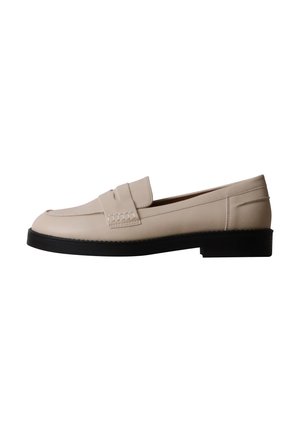Mocassin en cuir beige avec une semelle noire, un talon plat et une bride sur le dessus de la chaussure.
