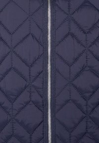 Giacca trapuntata blu navy con motivo a diamante, zip frontale argentata e tessuto strutturato. La chiusura con zip si estende centralmente sul davanti.