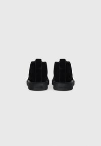 Stivaletti alla caviglia in suede nero con una finitura testurizzata, suola piatta in gomma nera e un design minimalista con linguette sul retro.