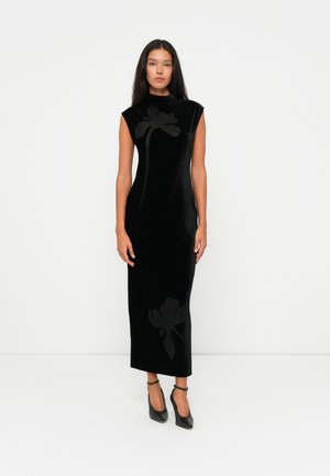 Vestito in velluto nero con silhouette aderente, collo alto e maniche a cappuccio. Presenta un sottile motivo floreale nero sul davanti.