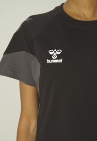 Čierne tričko s šedými akcentmi, s okrúhlym výstrihom a krátkymi rukávmi. Logo "hummel" je umiestnené na ľavej strane.