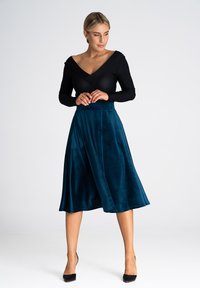 Czarna bluzka z długim rękawem w połączeniu z turkusową, miękką spódnicą do kolan w kształcie A. Gładki materiał z delikatnym połyskiem, zawiązanie w talii.