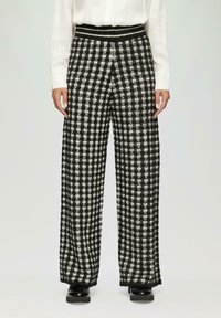 Zwart-witte geblokte broek met wijde pijpen van een textuurstof; elastische tailleband; zachte afwerking; gedragen met een witte blouse en zwarte schoenen.