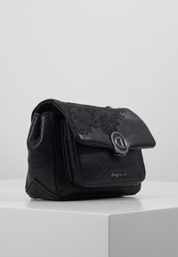 Černá syntetická kožená kabelka s květinovým krajkovým detailem, překlopným víkem, stříbrnými kovovými prvky a strukturovaným obdélníkovým tvarem.