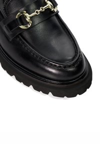 Black leather loafers with a rubber sole, featuring a metallic chain accent across the upper and detailed stitching along the edges.