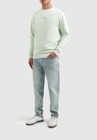 Lichtgroene sweatshirt, ronde hals, van katoen, met de tekst "PURE PATTI" op de borst. Gecombineerd met lichtblauwe jeans en witte sneakers.