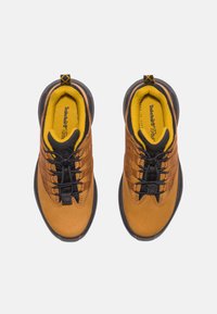 Scarpe da trekking marroni con tomaia liscia, lacci neri, fodera gialla e suola in gomma texturizzata. Presentano una punta arrotondata e fori rinforzati.