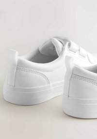 Zwei weiße Sneakers mit glatter Oberfläche und minimalistischem Design, auf einem hellen Hintergrund positioniert, die Ferse und Seitenansicht zeigend.