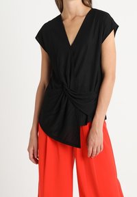 Svart wrap-top med korta ärmar, med en vriden framsidesdesign. Kombinerad med klara röda vida byxor, vilket skapar en djärv färgkontrast.