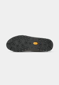Suola di scarpa in gomma nera con profonde scanalature e superficie texturizzata, con un logo arancione ben visibile. Progettata per aderenza e durata.