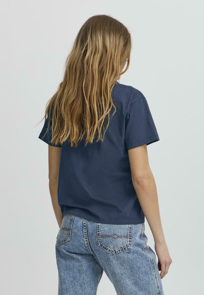 Námořnická modrá bavlněná tričko s krátkým rukávem a uvolněným střihem, spárované s vysoce pasovými vybledlými džíny s zadními kapsami.