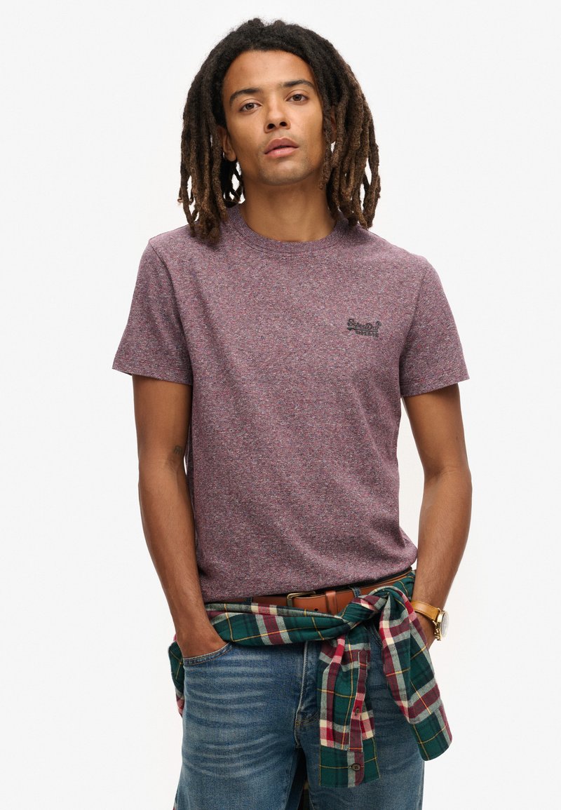 Korte mouw, ronde hals t-shirt in een maroon en grijze mélange stof, met een klein zwart logo. Draagt met blauwe jeans en een groen geruit shirt knopen in de taille.
