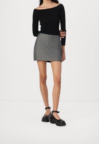 Zwarte geribbelde off-shoulder top gecombineerd met een grijze minirok met streepjes. Het model draagt chunky zwarte schoenen met enkelbandjes.