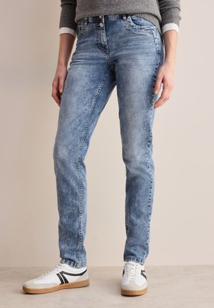 Lichtblauwe denim jeans met een vervaagde textuur, slim fit en twee voorkeurszakken, gecombineerd met witte sneakers met zwarte accenten.