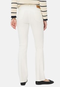 Witte flared jeans hebben een gladde textuur, een vijf-pocket ontwerp en gestikte details, gecombineerd met zwarte platte schoenen.