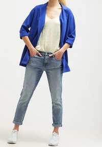 Modrá sako přes světle žluté tričko, doplněné světle modrými džíny a bílými teniskami. Sako má ohrnuté rukávy a volný střih.